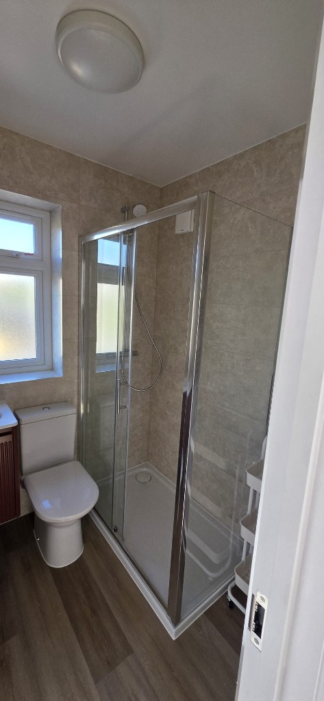 Complete ensuite bathroom refurbishment with glass shower, beige tiles and wood-effect floor by Ikveles Construction