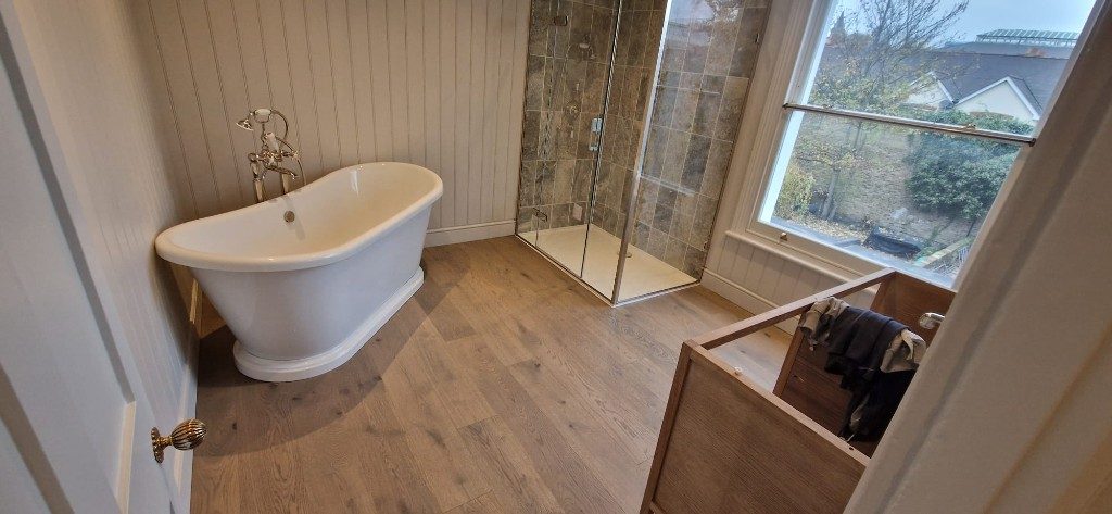 Spacious bathroom refurbishment with freestanding slipper bath, glass walk-in shower and wood flooring by Ikveles Construction