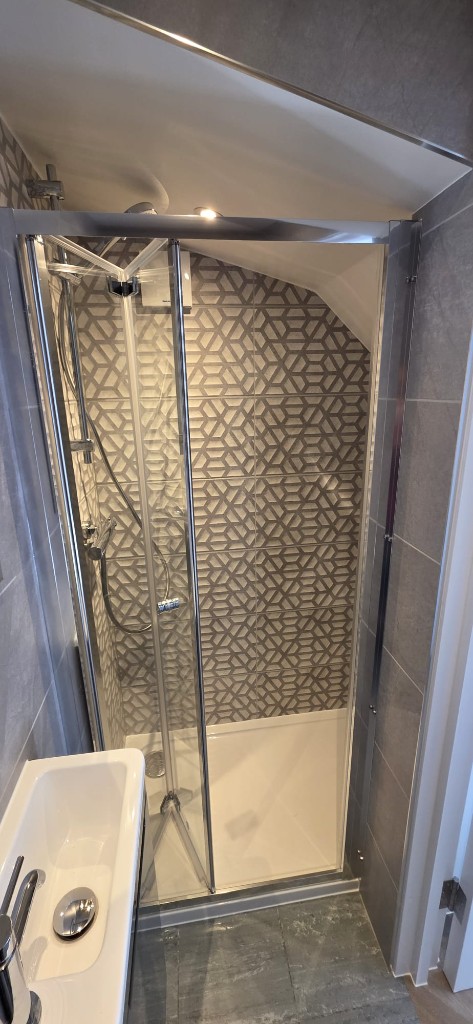 Compact bathroom shower with geometric feature tiles and bifold glass door by Ikveles Construction