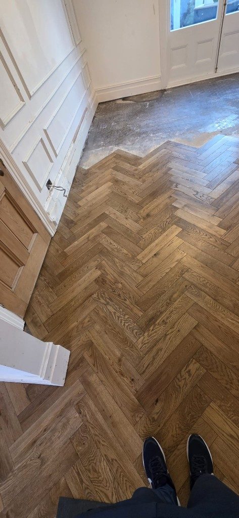 Herringbone wood flooring installation in progress with exposed subfloor by Ikveles Construction