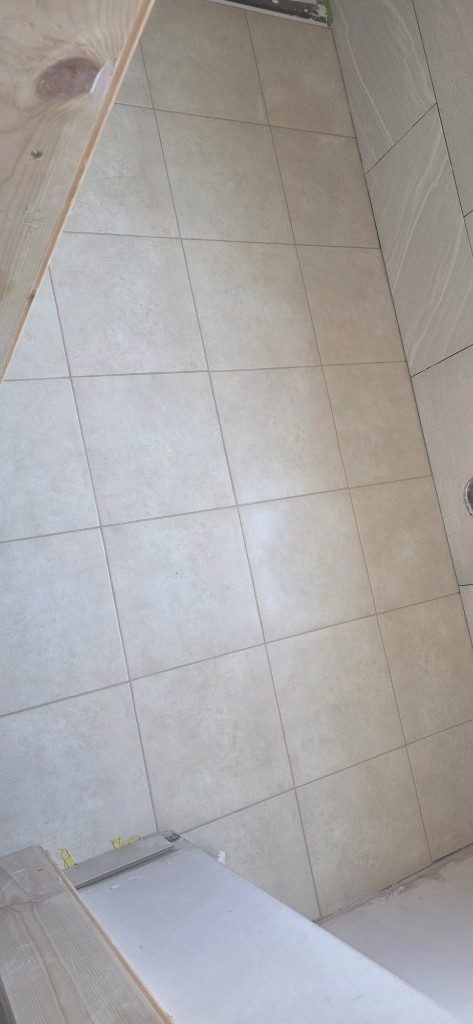 Bathroom tile installation with beige floor tiles and textured wall tiles by Ikveles Construction
