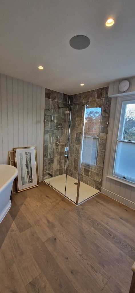 Stone-effect tiled walk-in shower with frameless glass by Ikveles Construction